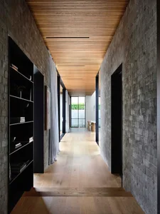 A modern corridor with brick walls and wooden flooring, featuring black-framed doors and large windows.