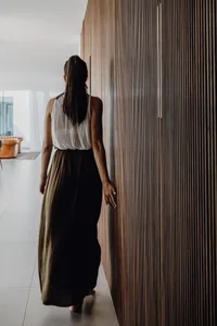 a woman wearing a white shirt and black skirt walking in front of a tall, striped wall, possibly in a modern or minimalist in