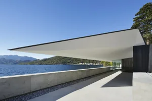 Modern architectural design featuring concrete and glass overlooking a waterfront.
