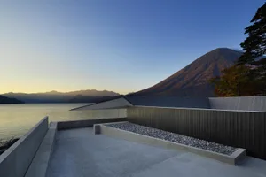 A modern concrete residence with a rooftop terrace overlooking a lake and mountains.