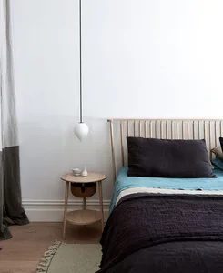 Bedroom with minimalist design featuring a wooden headboard, woolen blanket, and linen bedding on a wooden floor with a hangi