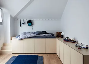 A minimalist bedroom with a wooden bed platform and a blue rug on a wooden floor.
