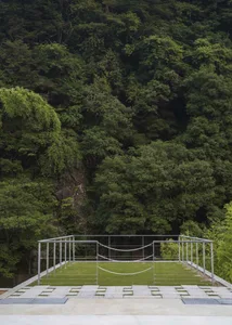 Minimalist architectural structure with metal frame and concrete platform surrounded by lush greenery in a forest setting.