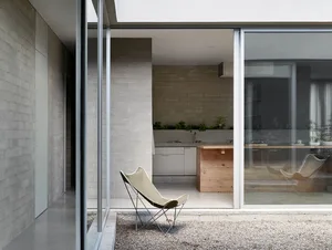 Modern minimalist residential kitchen with concrete walls and flooring, featuring a small island with a wooden countertop.