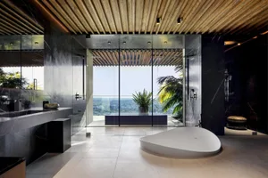 A modern bathroom with large glass windows showcasing an urban view, featuring sleek black marble accents and a large freesta