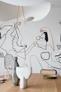 A modern dining room featuring ceramic tableware and a mural of abstract figures on the wall.