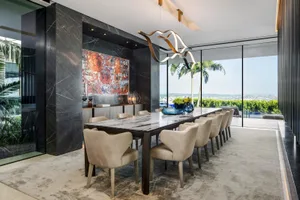 A modern dining room featuring a marble table, upholstered chairs, and a contemporary light fixture.