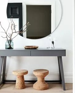 A minimalist entryway featuring a wooden console table with a stool, a round mirror, and a hemp plant in a vase.