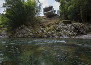 A modern concrete house built on a steep hillside overlooking a river.