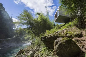 A modern house designed with concrete, timber, and glass materials located in a forested area.