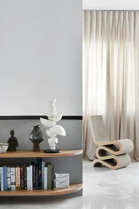 A modern living room features a curved wooden bookshelf with marble accents, a contemporary white sculpture, and a fabric-cov