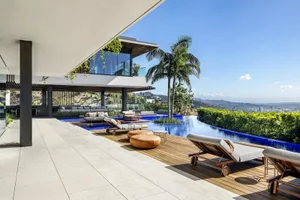 Modern luxury house with a large infinity pool, wooden deck, and tropical palm trees.