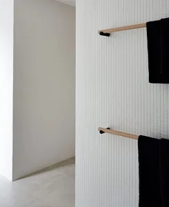 A modern minimalist bathroom with white ceramic tiles and black towels hanging on a wooden rack.