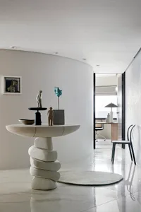 A modern minimalist entryway featuring a concrete table with various sculptures on top, set against a white wall and floor.