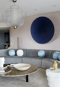 A modern minimalist living room with a curved gray sofa adorned with light blue cushions, a round coffee table with a stone t