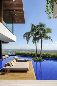A modern pool deck with a palm tree, lounge chairs, and a cityscape view.