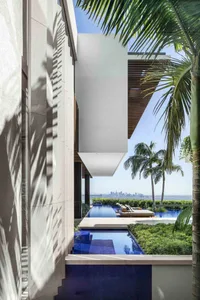 Modern, minimalist architecture featuring a sleek, glass and concrete poolside setting with a view of a city skyline.