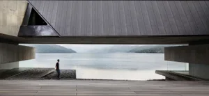 Person standing on a wooden platform overlooking a calm lake surrounded by mountains.
