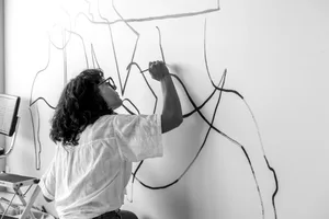 Woman drawing a black and white line art on a white wall with chalk.