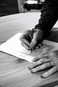 A hand with a pencil drawing on a sheet of paper with a design diagram on it.