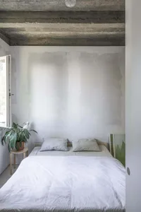 Sparse bedroom with concrete ceiling, white bedding, and minimalist design.