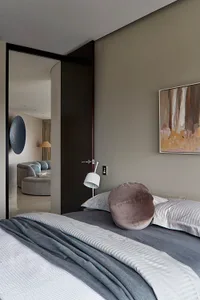 A minimalist bedroom with grey and taupe tones, featuring a bed, pillows, and a painting.