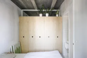 Minimalist bedroom with wooden cupboards and green potted plants on top.