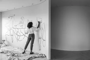 A woman artist painting minimalist figures on a white wall.