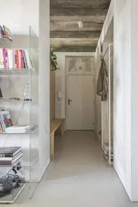 Modern minimalist entryway with wooden bench, glass bookshelf, and concrete ceiling.