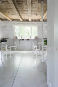 Modern minimalist kitchen with concrete flooring, wooden ceiling beams, metal accents, and a seafoam green wall.