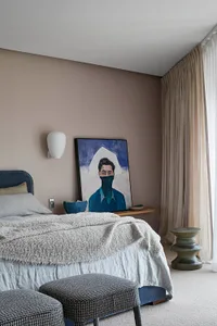 A modern bedroom featuring a bed with gray bedding, a dark blue bed frame, and a hanging sconce above it, alongside a portrai