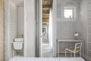 Modern minimalist bedroom with concrete walls, wood accents, and white furniture.