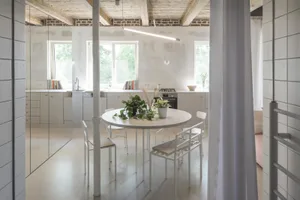 A minimalist kitchen and dining area with a round table, chairs, and plants.