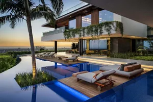 Modern house exterior with glass and concrete materials, featuring a pool and lounge area.