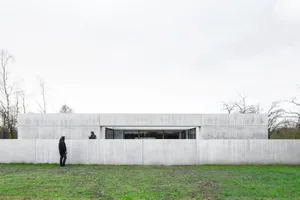 A minimalist house with a concrete facade, featuring large windows and a simple, sleek design.