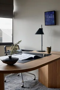 A modern office desk space featuring a wooden desk with a lamp, a sketchbook, and a chair.