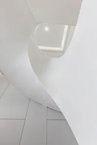 A minimalist white staircase illuminated by natural light from a square skylight.