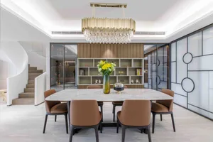 A modern dining room with a marble table and chairs, featuring a chandelier and bookshelf.