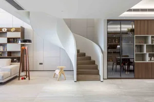 A modern residential interior featuring a stylish spiral staircase and a reading area with a glass cabinet and bookshelves.