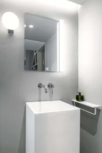 A minimalist industrial bathroom featuring a white ceramic sink with chrome faucet and a rectangular mirror with a light fixt