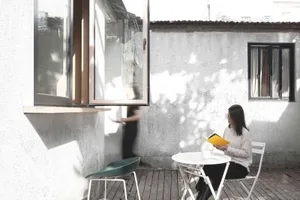 A woman sitting at a table reading a book in a minimalist home exterior with concrete walls.