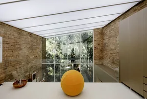 An interior space with brick walls, large glass windows, and a yellow ball on the floor.
