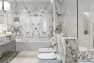 Modern bathroom featuring marble walls and floor, white fixtures, and contemporary design elements.