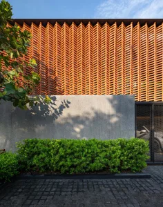Modern house exterior with wooden lattice, concrete walls, and green hedge.