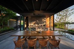 Modern industrial dining room with wooden furniture, marble walls, and glass windows overlooking a serene water feature.