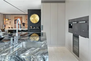 Modern kitchen featuring a marble countertop with stainless steel appliances and a circular golden light fixture.