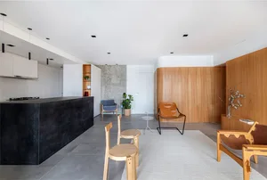 A modern living room with a concrete island, wooden chairs, and a leather lounge chair.