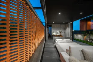 Modern minimalist bedroom with wood and concrete interior, featuring a bed and a reading lamp. Nighttime view.