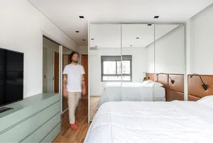 A modern minimalist bedroom with large floor-to-ceiling mirrors, white bed linens, and wooden flooring.