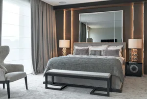 A modern minimalist bedroom featuring a grey upholstered bed, a bench, and two台 lamps, all set against a wall of mirrors and 
